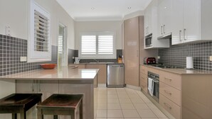A modern kitchen with a central island, stainless steel appliances, and a tiled backsplash. - Bennett’s Beach Townhouse (Hawks Nest)