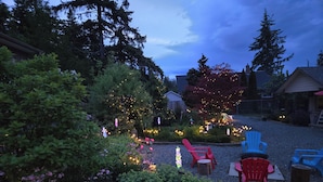 A garden with various plants and trees, outdoor seating with chairs, and decorative lights.