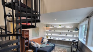 A modern living room with a black spiral staircase, a blue sofa, and a bookshelf filled with decorative items.