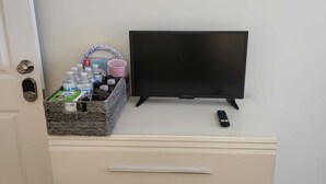 Een televisie op een dressoir met een afstandsbediening, een mandje met toiletartikelen en een deur met slot.