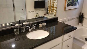 Een badkamer met een zwarte countertop, een witte wastafel en een grote spiegel. Er is een douche zichtbaar op de achtergrond, en een lijst met een schilderij aan de muur.