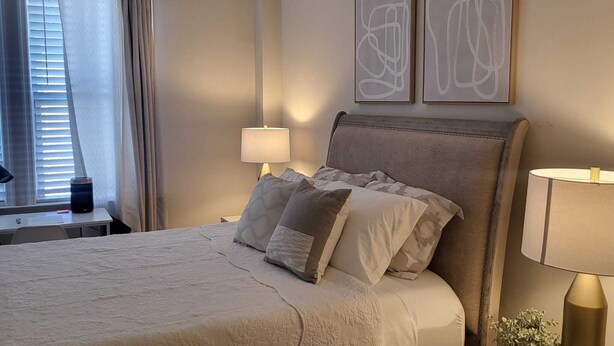 Een netjes ingerichte slaapkamer met een bed, bedlampen, een nachtkastje en een raam met gordijnen.