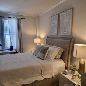Un dormitorio ordenado con cama, lámparas de noche, mesita de noche y ventana con cortinas.