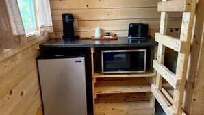 Een kleine keuken met een koelkast, magnetron en houten planken.