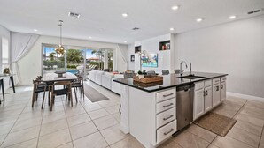 A modern kitchen with a central island, white cabinetry, and a large window offering a view of the outdoors. - The Villa Tranquility with Private Pool (Kissimmee)