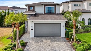 A modern two-story house with a garage, surrounded by well-maintained landscaping and palm trees. - The Villa Tranquility with Private Pool (Kissimmee)
