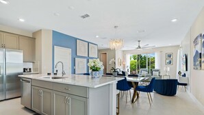 A modern kitchen with a central island, stainless steel appliances, and a dining area with blue chairs. - Blue Suede Townhome in Reunion Resort (Kissimmee)