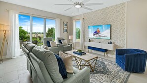 A modern living room with a sofa, armchairs, a coffee table, and a TV mounted on the wall. - Blue Suede Townhome in Reunion Resort (Kissimmee)