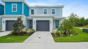 A modern two-story house with a blue and gray exterior, two garage doors, and a well-maintained front yard with grass and small plants. - Blue Suede Townhome in Reunion Resort (Kissimmee)