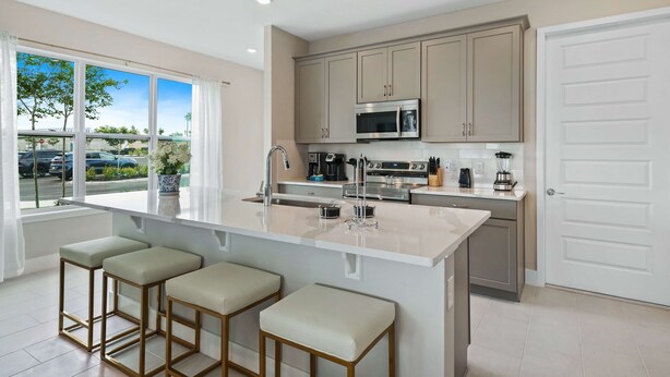 A modern kitchen with a large island, bar stools, and a view of the parking lot. - Blue Suede Townhome in Reunion Resort (Kissimmee)