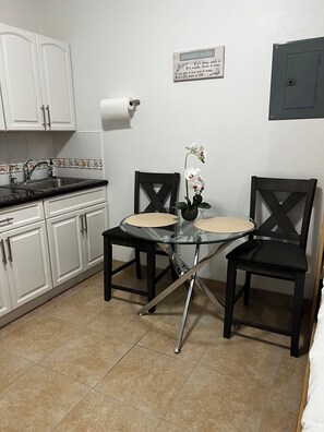 A kitchen with white cabinets, a sink, a glass table with chairs, and a kitchen rules sign on the wall.