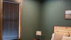 A bedroom with a bed, a ceiling fan, a window with blinds, a nightstand with a lamp, and a framed picture on the wall. - Cozy Lodge at Ward Creek Ranch close to interstate and wedding venues.  (Simms)