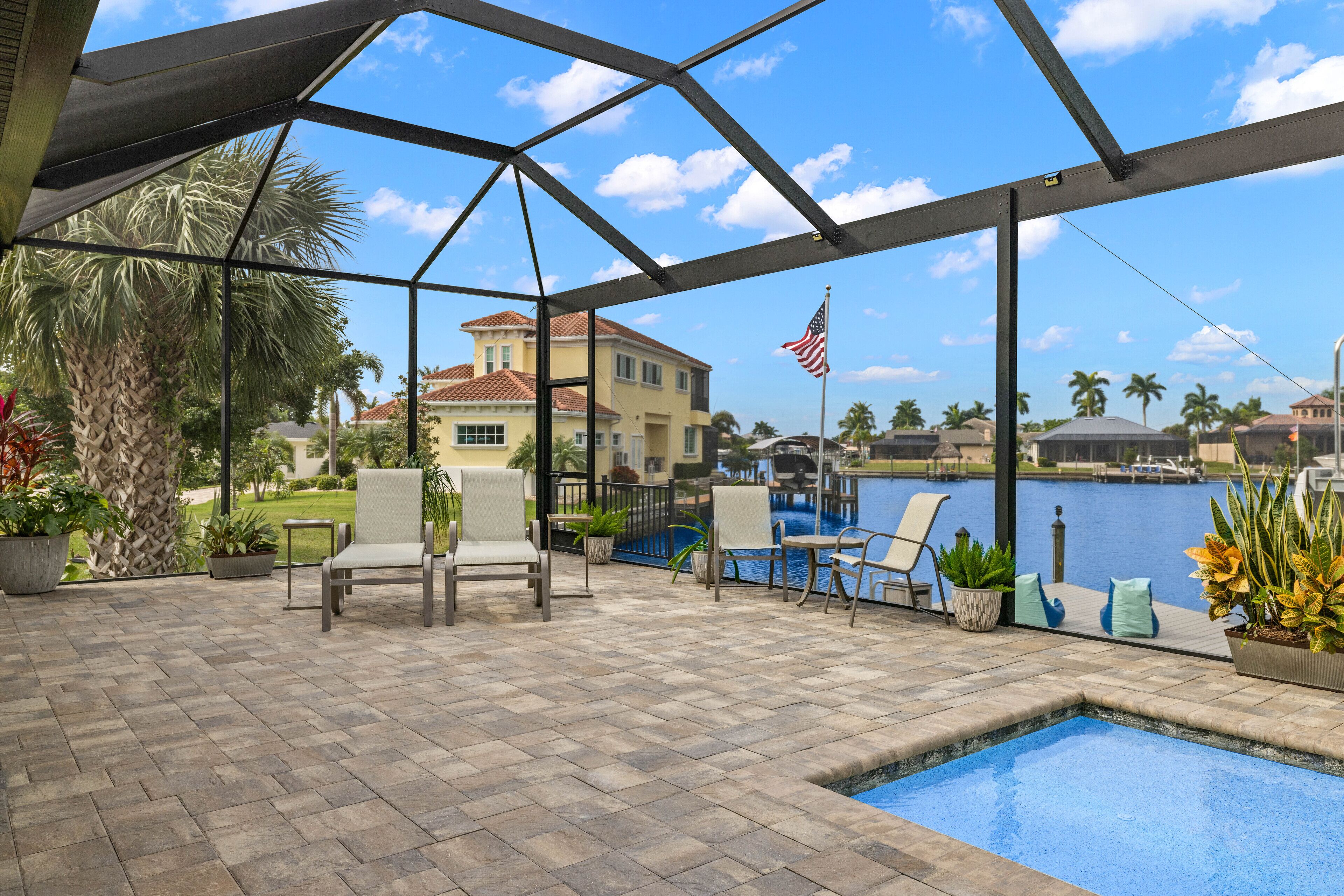 A covered outdoor area with a pool, chairs, and potted plants.