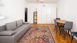 Un salon moderne avec un canapé gris, un tapis à motifs, une table à manger en bois avec des chaises et une armoire blanche.