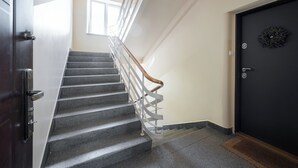 Un escalier avec une rampe, une porte sombre et un paillasson.