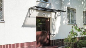Un bâtiment blanc avec une porte marron, un petit porche et une rambarde en métal.