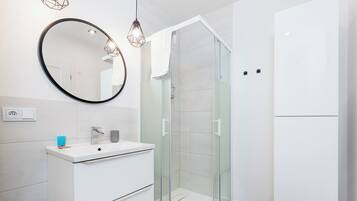 Een moderne badkamer met een douchecabine van glas, een witte wastafel met spiegel en hanglampen.