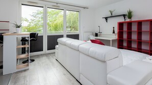 A modern living space with a white sofa, a red shelving unit, a small desk, and a sliding glass door leading to a balcony.