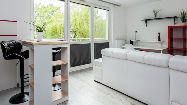 A modern living space with a white sofa, a black chair, a wooden desk, and a red shelving unit.