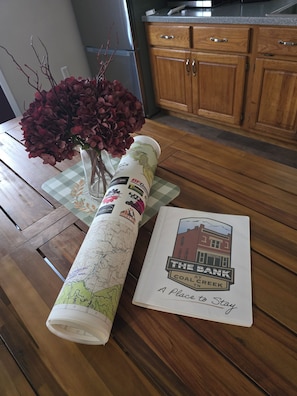 En ihopvikt karta med en tryckt skylt där det står ”The Bank at Coal Creek” och en liten vas med röda blommor på ett träbord.