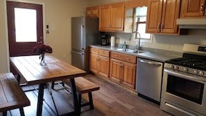 Una cocina con armarios de madera, electrodomésticos de acero inoxidable, una mesa de madera con bancos y una ventana que proporciona luz natural.