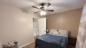 Un dormitorio con cama, ventilador de techo, mesita de noche y un vestidor.