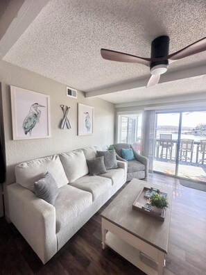 A living room with a beige sofa, a coffee table, and artwork on the wall. - Lakefront main channel views! Boat slip! (Osage Beach)
