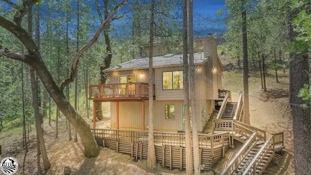 Une cabane en bois à deux étages, dotée d’un balcon et entourée d’arbres.