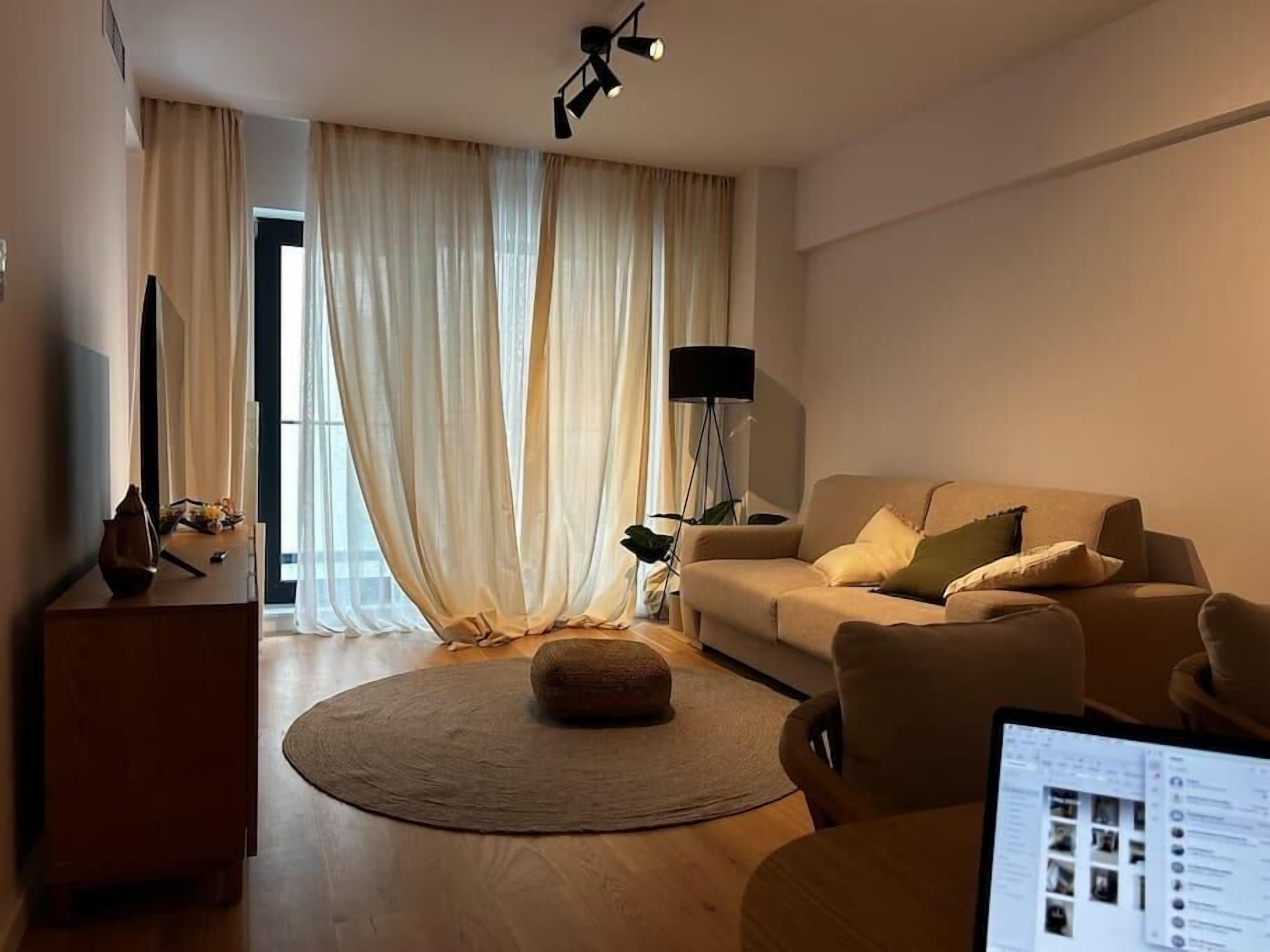 A modern living room with a sofa, ottoman, and a laptop on a table.