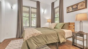 Ein Schlafzimmer mit Bett, Nachttischlampen, einem Nachttisch und einem Fenster mit Vorhängen.