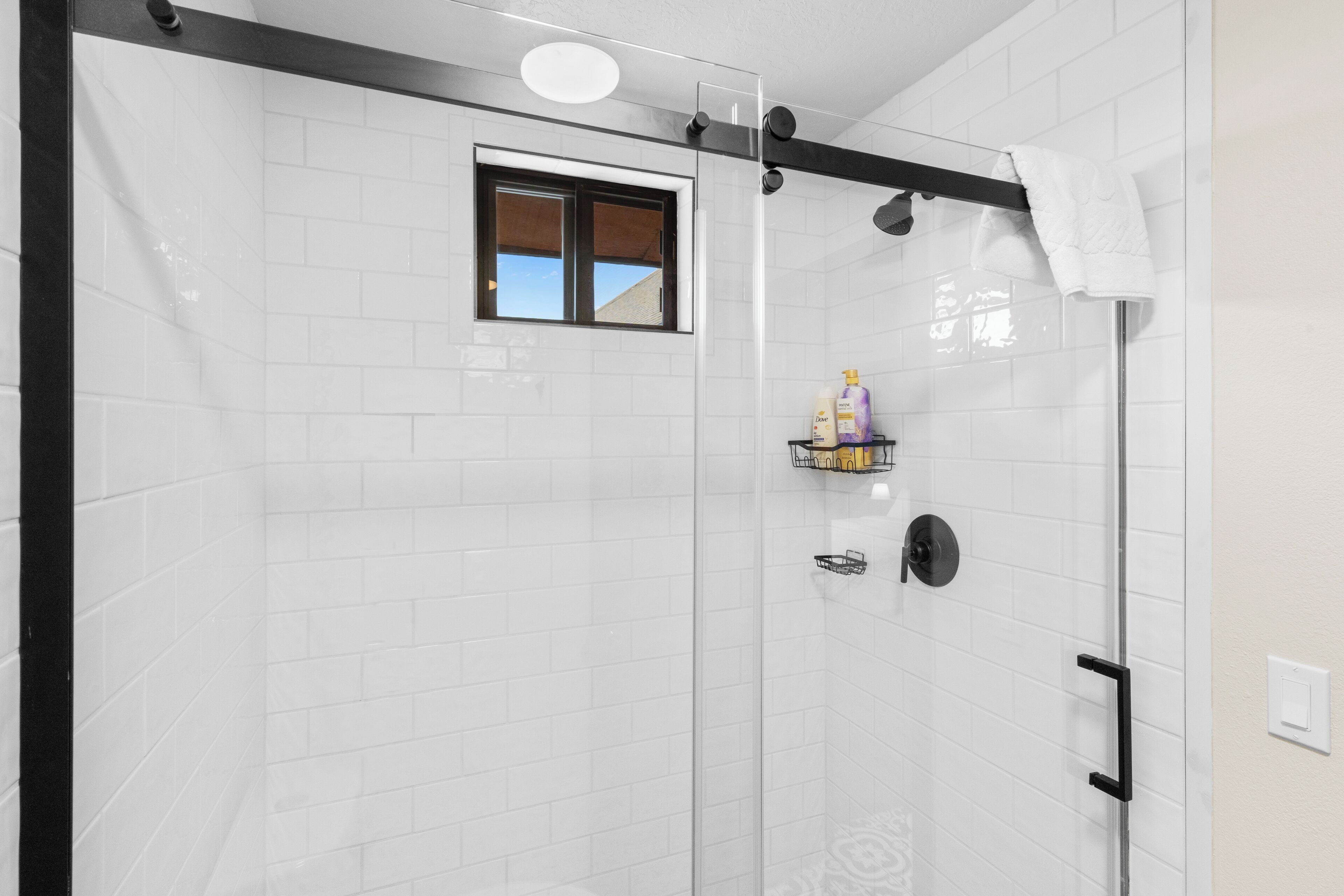 A glass-enclosed shower with white tiles, a window, and a towel rack.