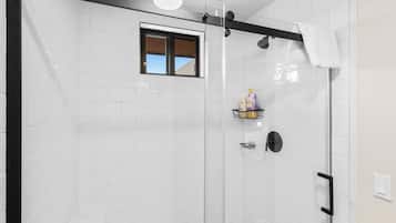 A glass-enclosed shower with white tiles, a window, and a towel rack.