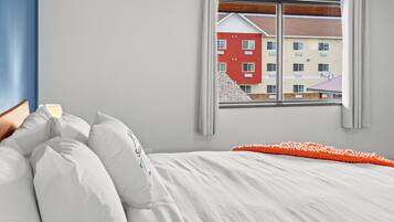 Une chambre à coucher avec un lit, des oreillers, une fenêtre donnant sur des immeubles et un mur bleu.