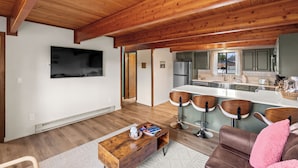 A modern kitchen with a wooden ceiling, a large island with bar stools, and a dining area with a sofa and a coffee table. - Owl's Nest (West Yellowstone)