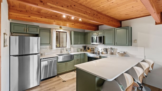 A modern kitchen with green cabinets, stainless steel appliances, and a wooden ceiling. - Owl's Nest (West Yellowstone)