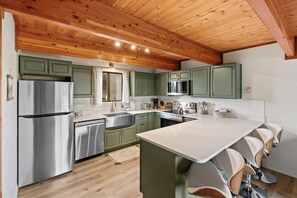 A modern kitchen with green cabinets, stainless steel appliances, and a wooden ceiling. - Owl's Nest (West Yellowstone)