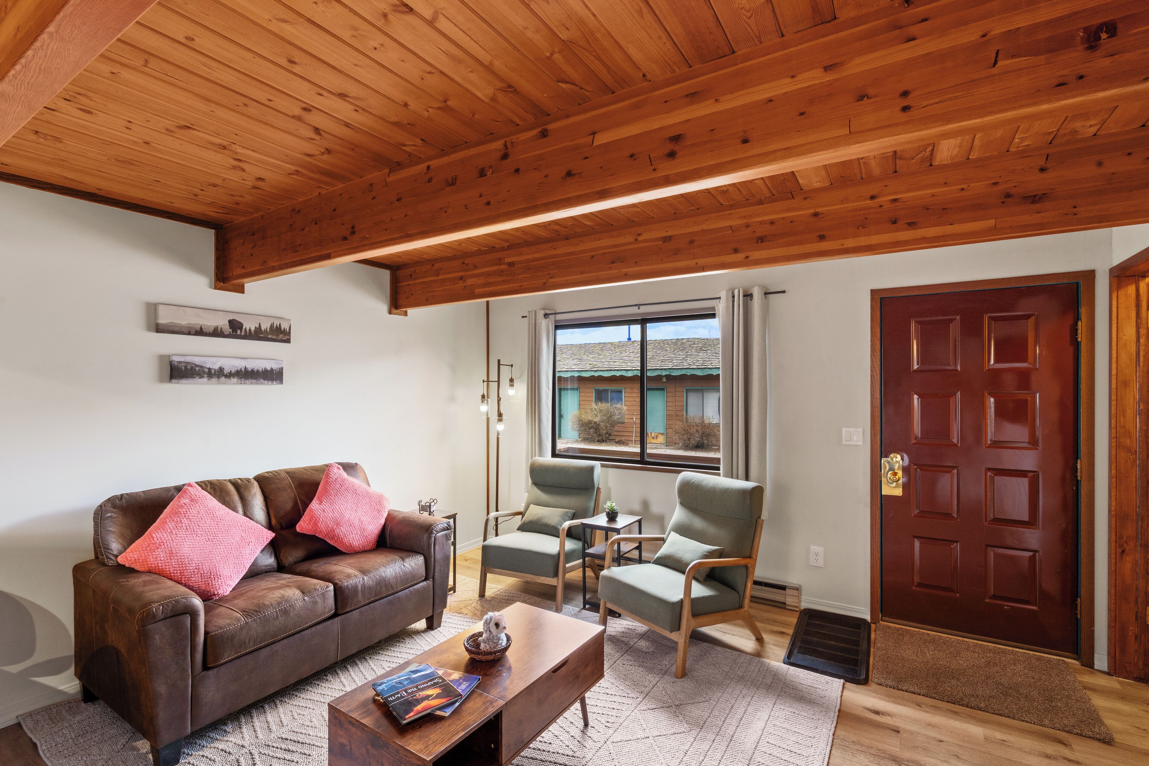 Una sala de estar con un sofá de cuero marrón, dos sillones verdes, una mesa de centro de madera y techo de madera.