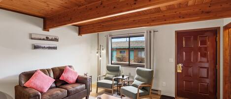 Una sala de estar con un sofá de cuero marrón, dos sillones verdes, una mesa de centro de madera y techo de madera.