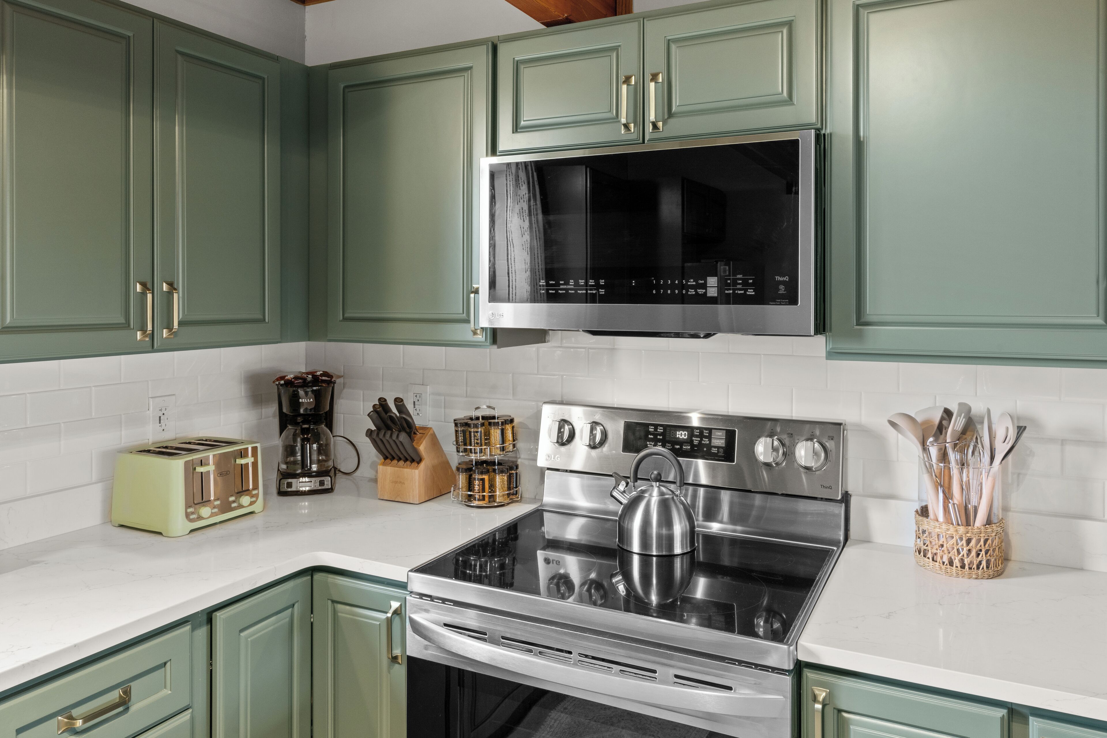 A kitchen with green cabinets, a stainless steel stove, a microwave, a toaster, and a coffee maker.