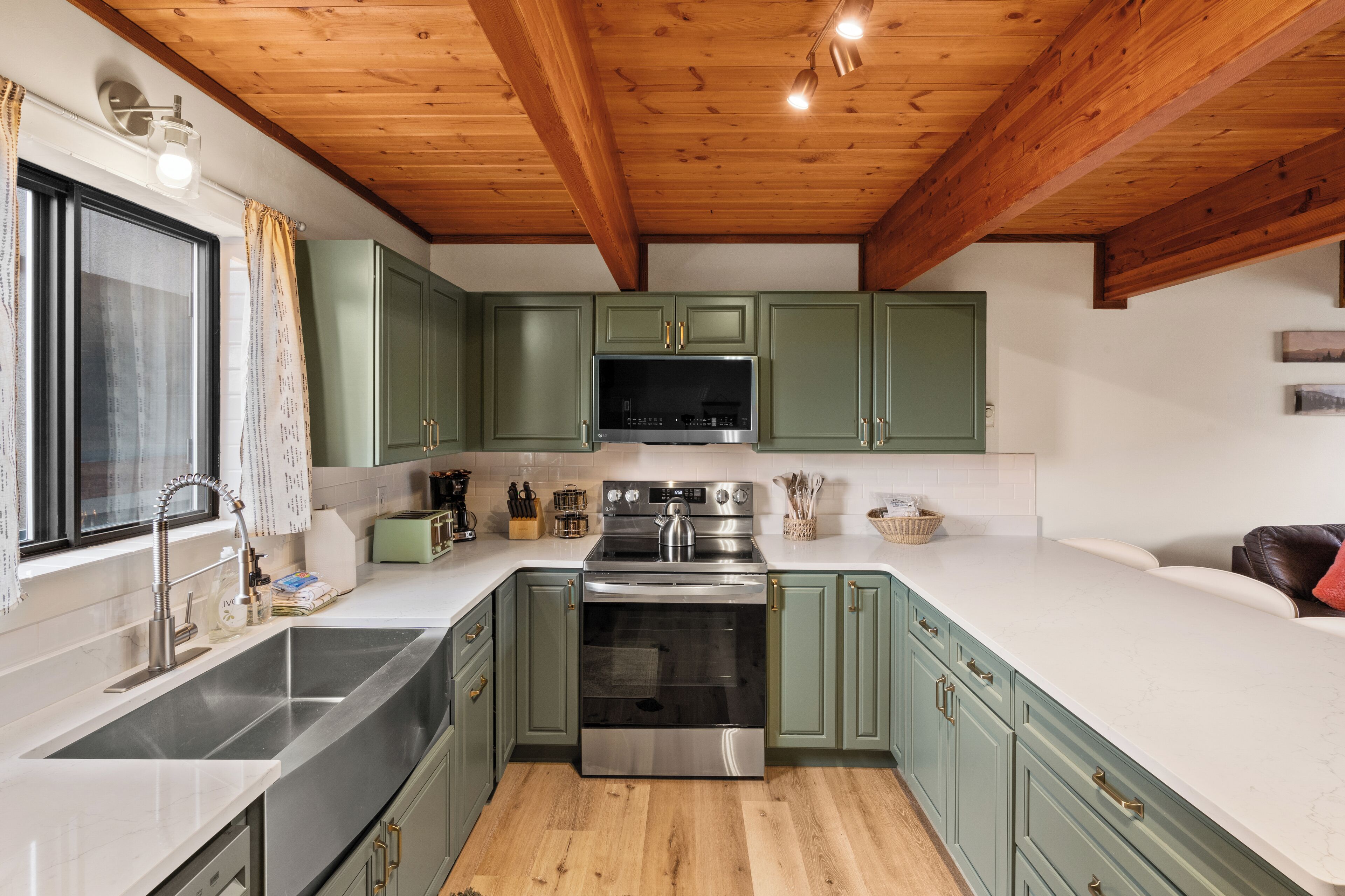 A kitchen with green cabinets, a stainless steel sink, and a built-in oven.