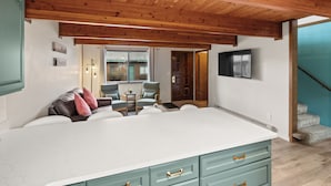 A spacious kitchen with a large island, wooden ceiling beams, and a view of the outside. - Owl's Nest (West Yellowstone)