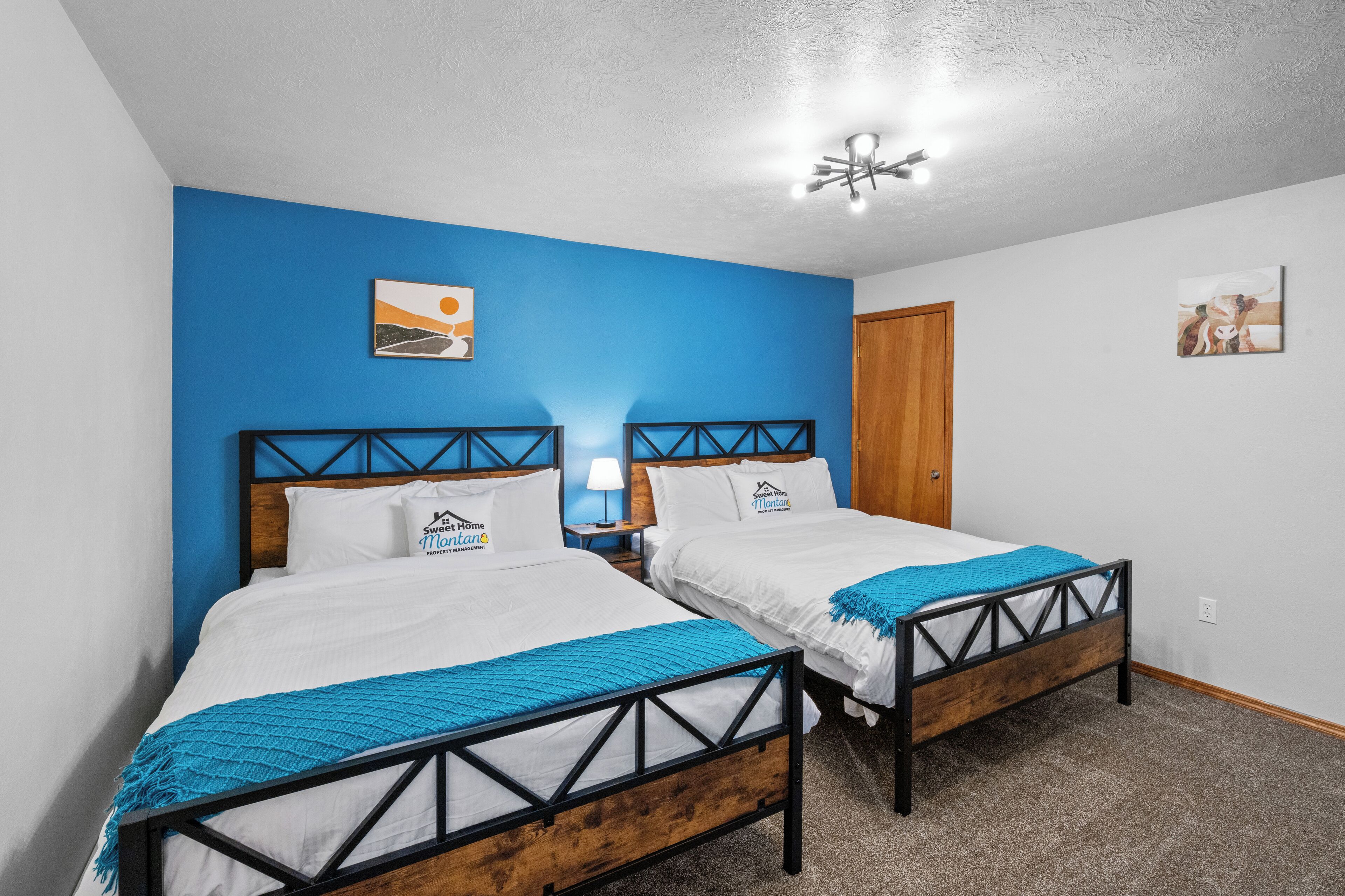 Una habitación con dos camas, una puerta de madera y una pared azul decorativa.