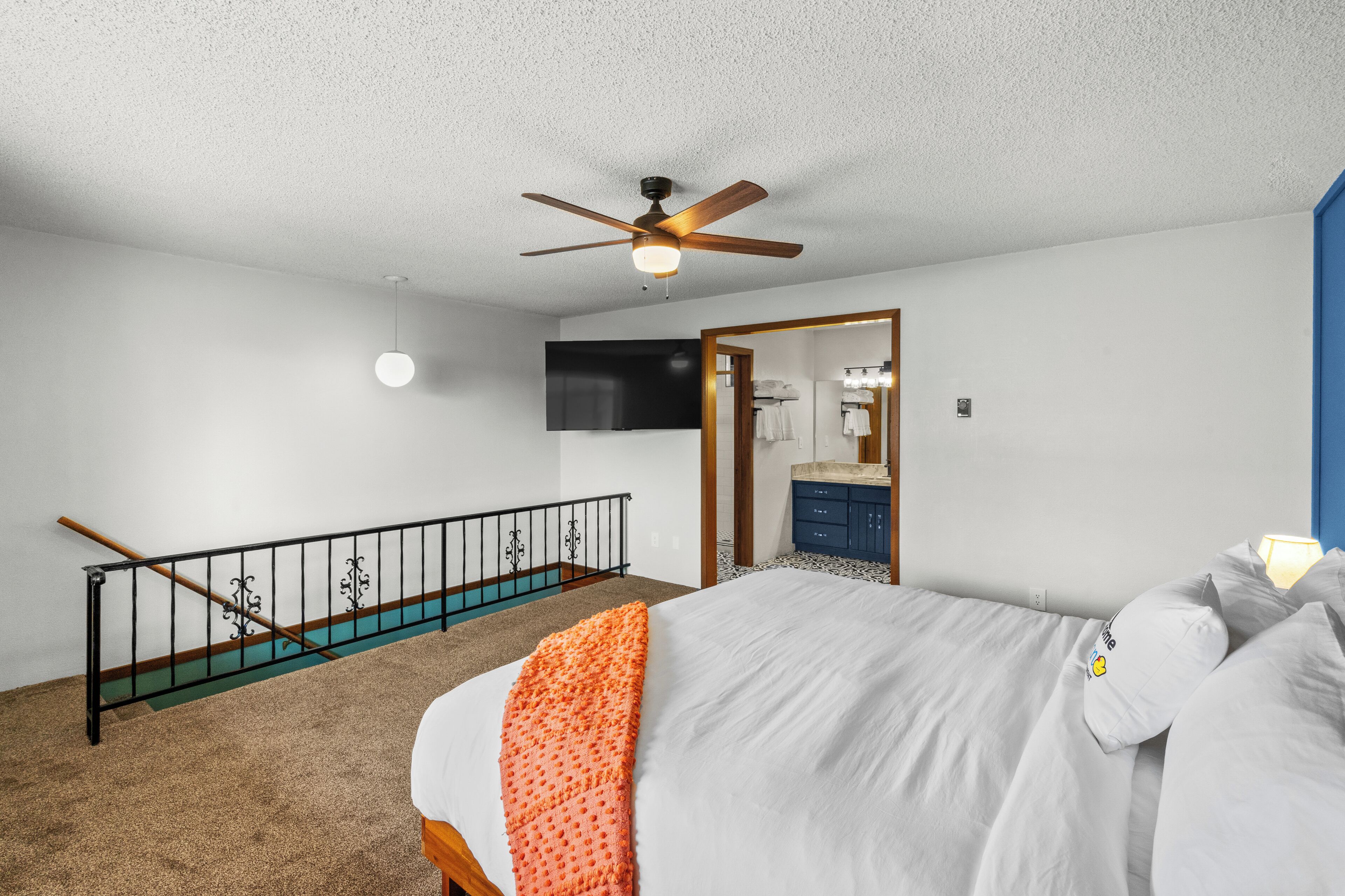 A bedroom with a bed, a ceiling fan, a staircase, and a bathroom visible through an open door.
