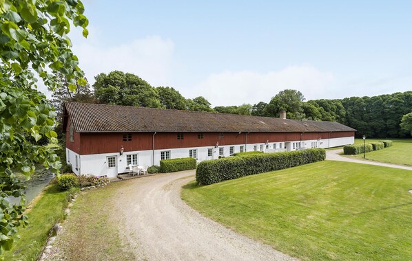 A large, single-story barn with a red and white exterior, surrounded by a well-maintained lawn and a gravel path leading to the entrance.