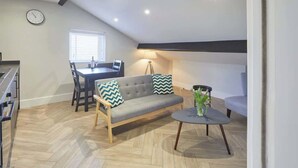 A modern loft apartment with a dining area, sofa, and a small round table with a vase. - Grace’s Loft - Central Scarborough 1 Bed Apartment (Scarborough)