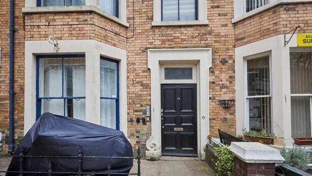 A corner building with a black door, a covered car, and a sign indicating a sublet. - Grace’s Loft - Central Scarborough 1 Bed Apartment (Scarborough)