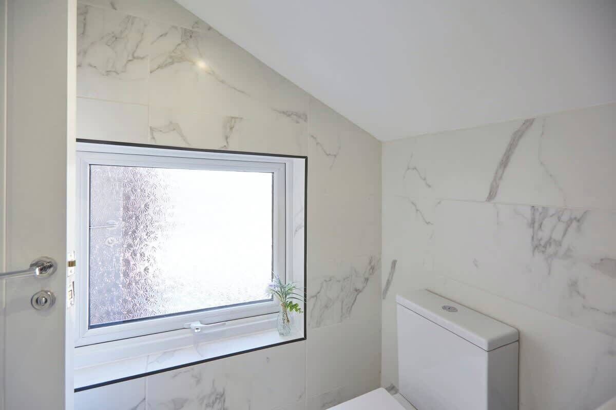 Une salle de bain avec des murs en marbre, une fenêtre à verre dépoli et des toilettes.