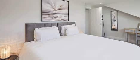 A bedroom with a large bed, a bedside table with a lamp, and a framed picture on the wall.