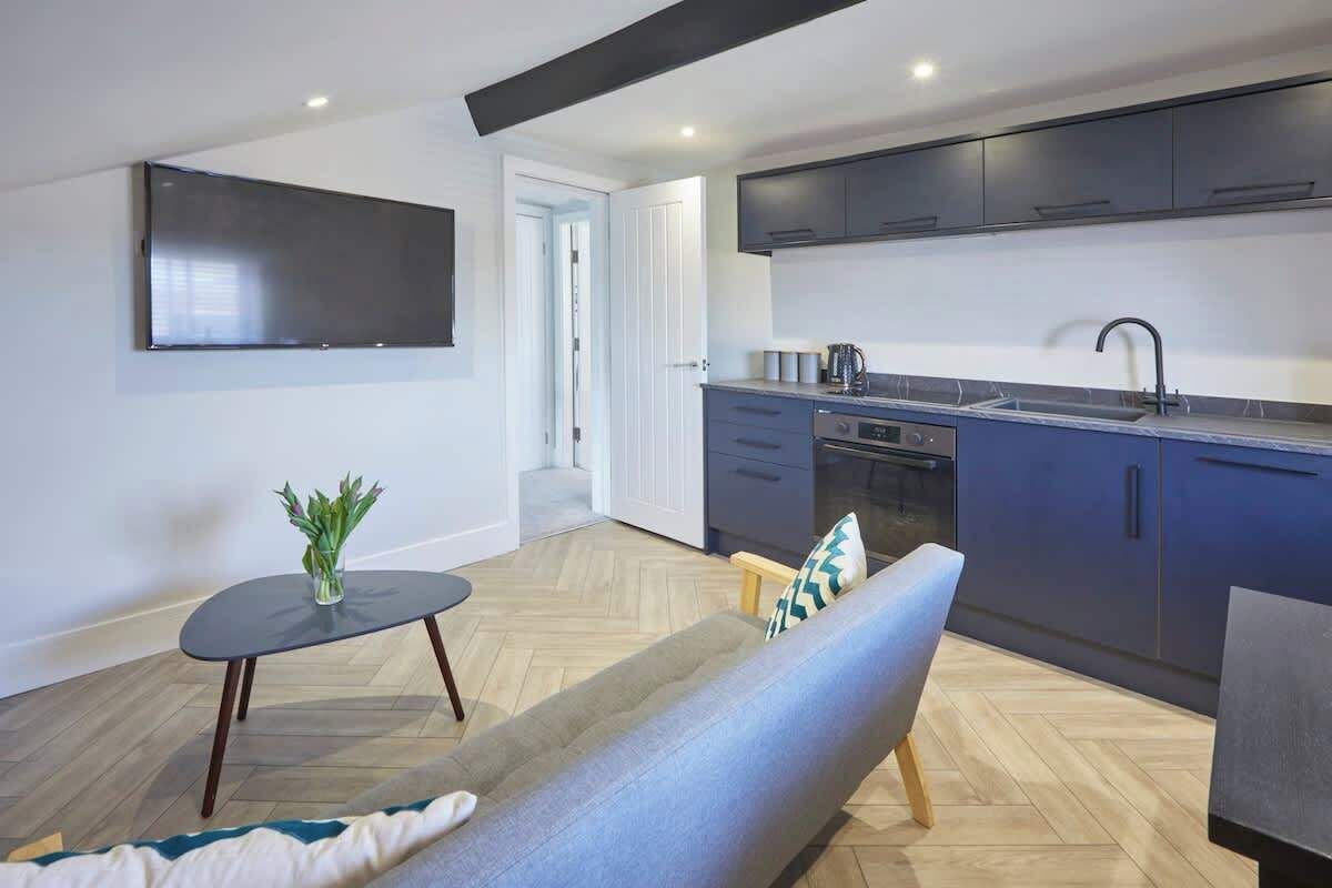 A modern living room with a sofa, a small table with a plant, and a TV mounted on the wall.