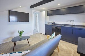 A modern living room with a sofa, a small table with a plant, and a TV mounted on the wall. - Grace’s Loft - Central Scarborough 1 Bed Apartment (Scarborough)